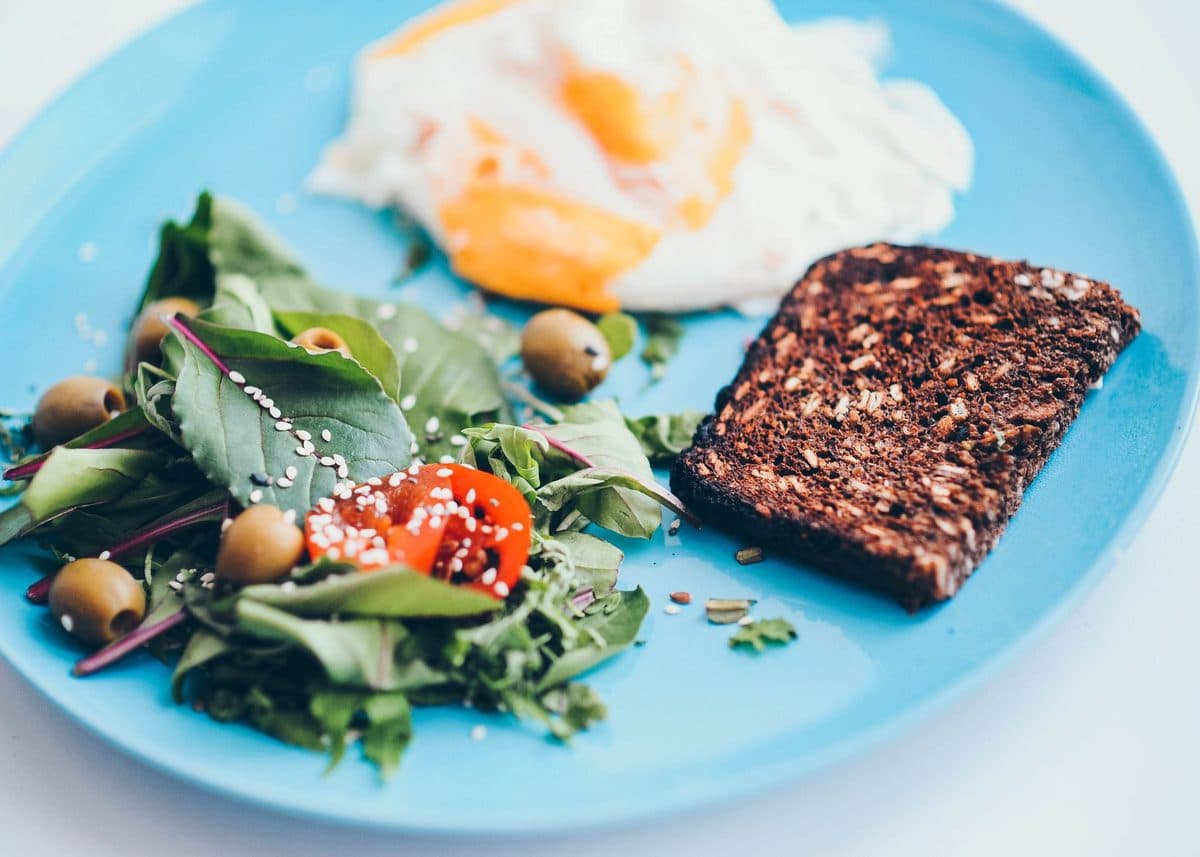 Prato colorido com salada, grãos e proteína grelhada sobre uma mesa de madeira clara