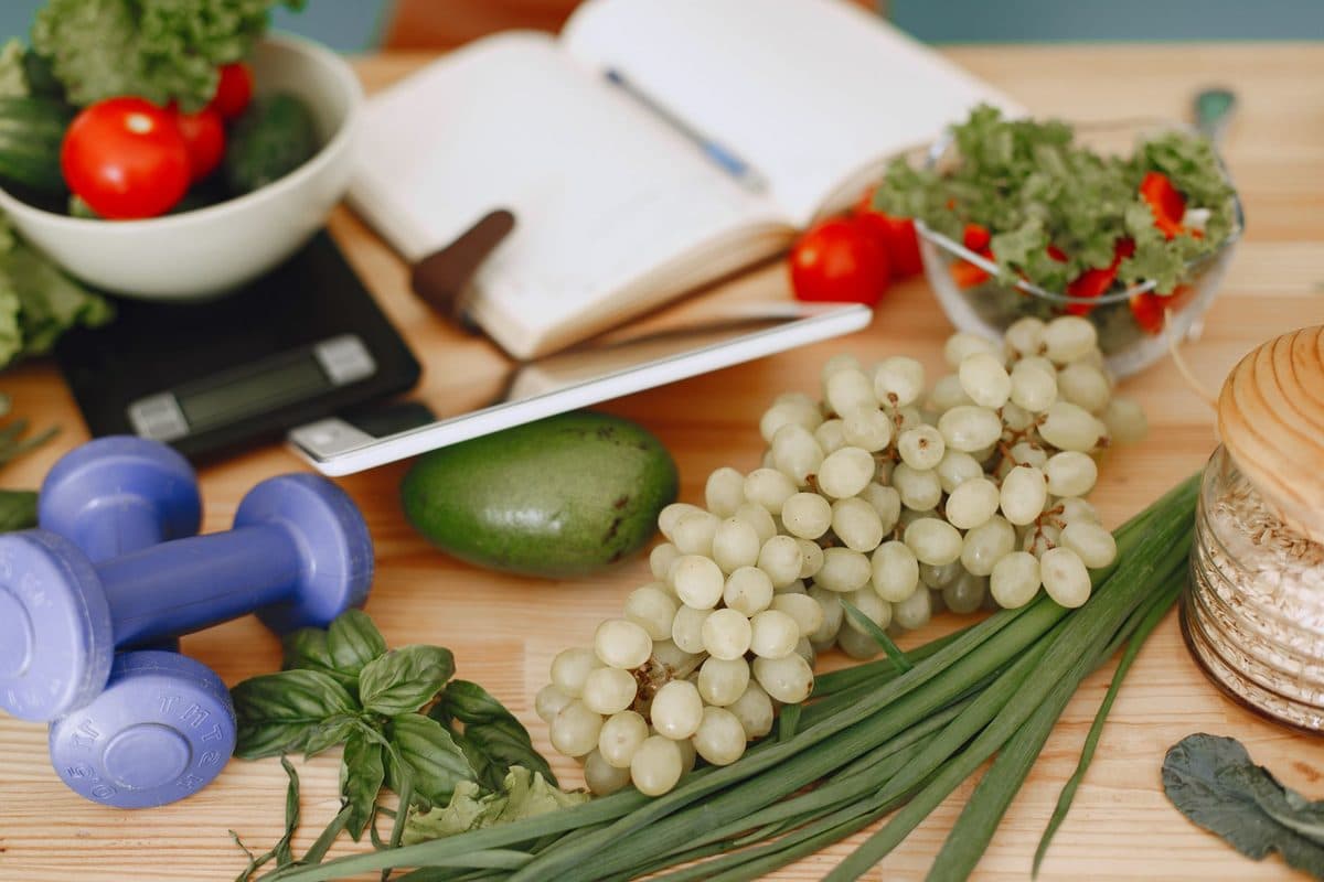Balança de cozinha ao lado de vegetais frescos, frutas e grãos integrais sobre bancada clara