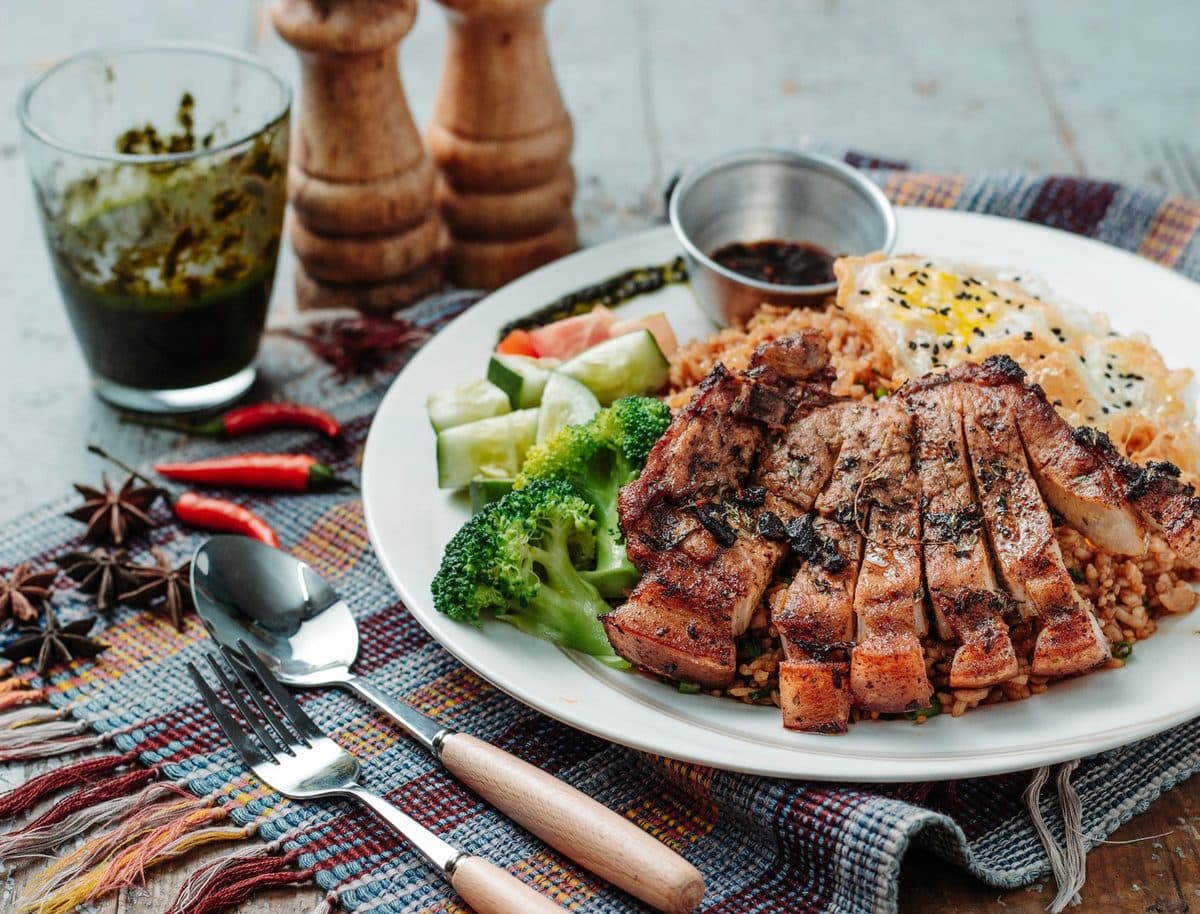Prato com peito de frango grelhado, arroz integral, ovos e brócolis ao lado de uma garrafa de água