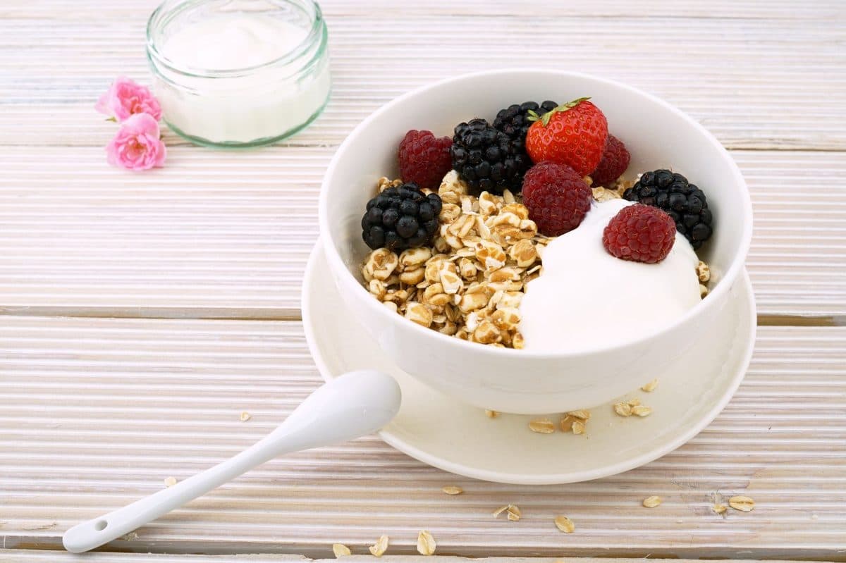 Tigela de aveia com frutas vermelhas, sementes e iogurte ao lado de um copo de água sobre mesa clara